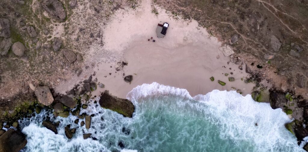 Aerial top view of Al Fazayah Beach in Salalah, Oman with waves hitting the sandy shore