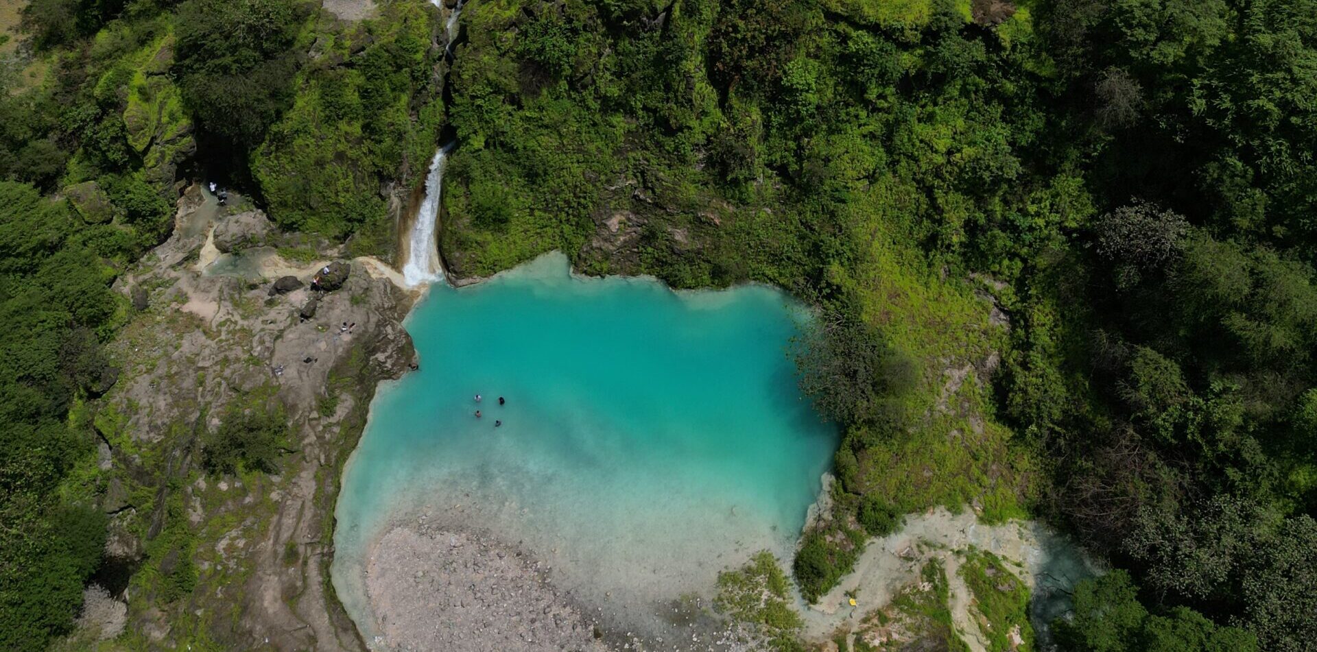 Aerial view of Wadi Jarziz in Salalah, Oman during Khareef season with turquoise lagoon and waterfall