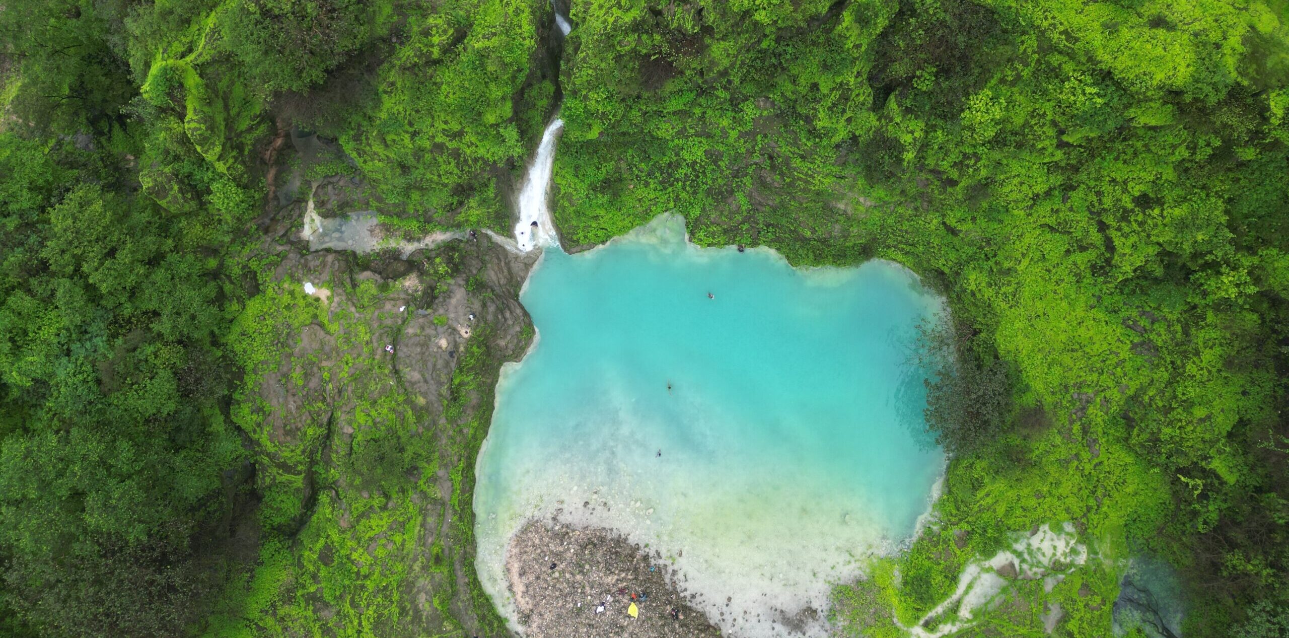Aerial view of Wadi Jarziz in Salalah, Oman during Khareef season with turquoise lagoon and waterfall