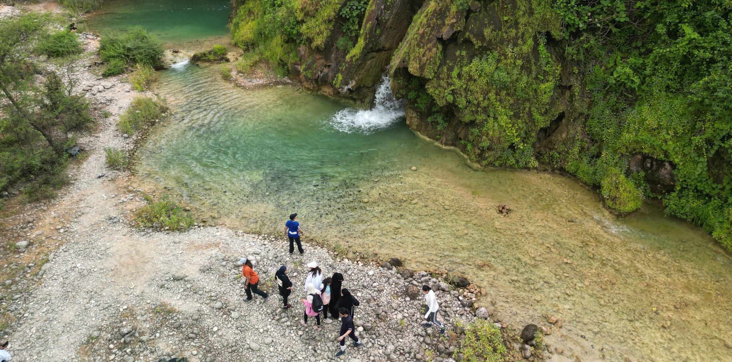 Group hiking at Wadi Jarziz in Salalah, Oman during Khareef season with waterfall and clear stream