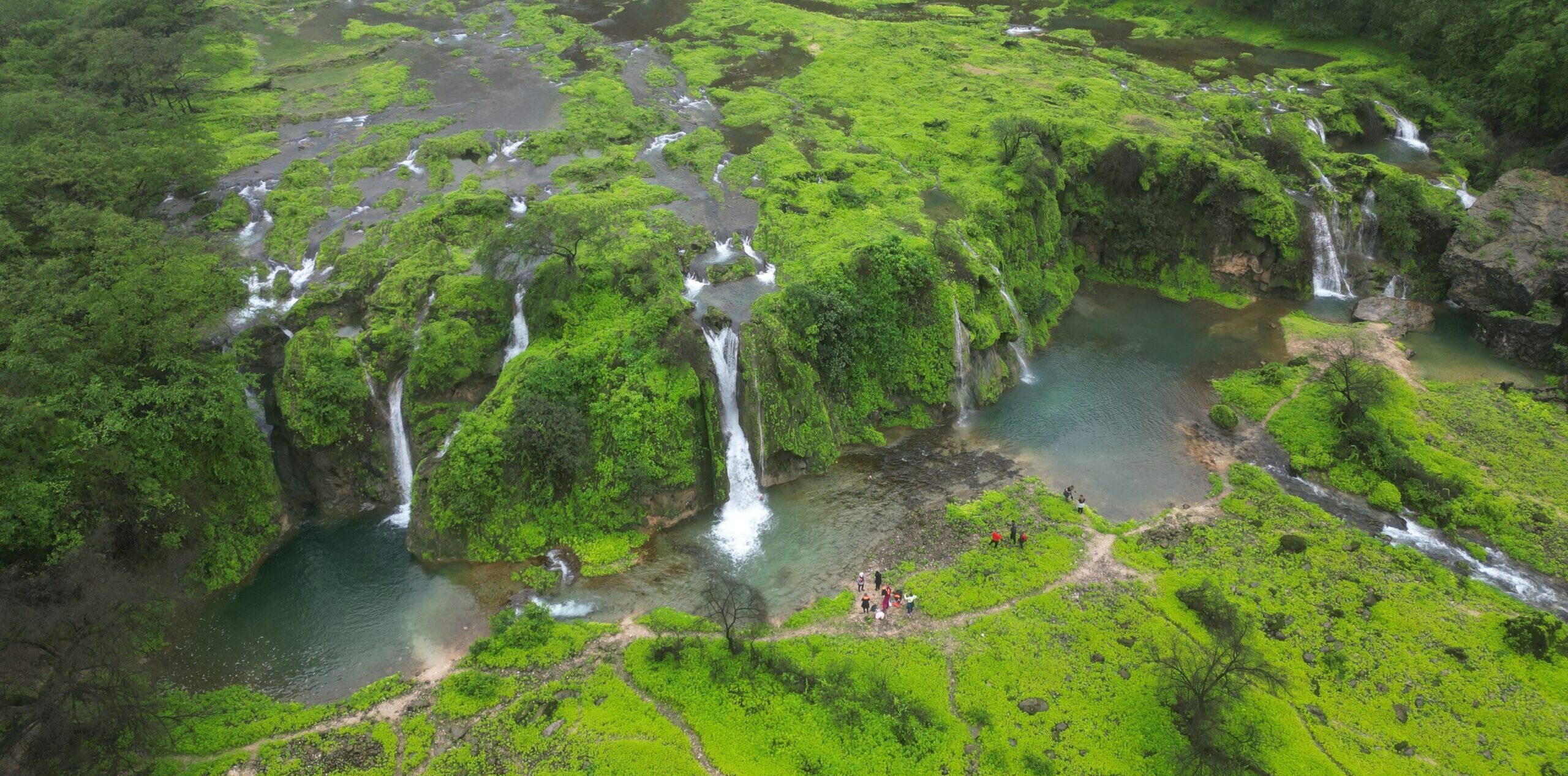 Group hiking at Wadi Jarziz in Salalah, Oman during Khareef season with green valley and stream