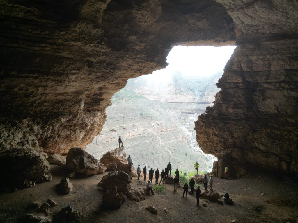 Group of hikers inside a hidden cave in Salalah Oman with mountain view and natural rock formations