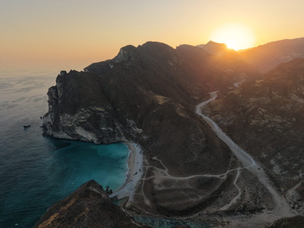 Hidden Beach Salalah Oman sunset view with mountains, turquoise sea, and scenic coastal road