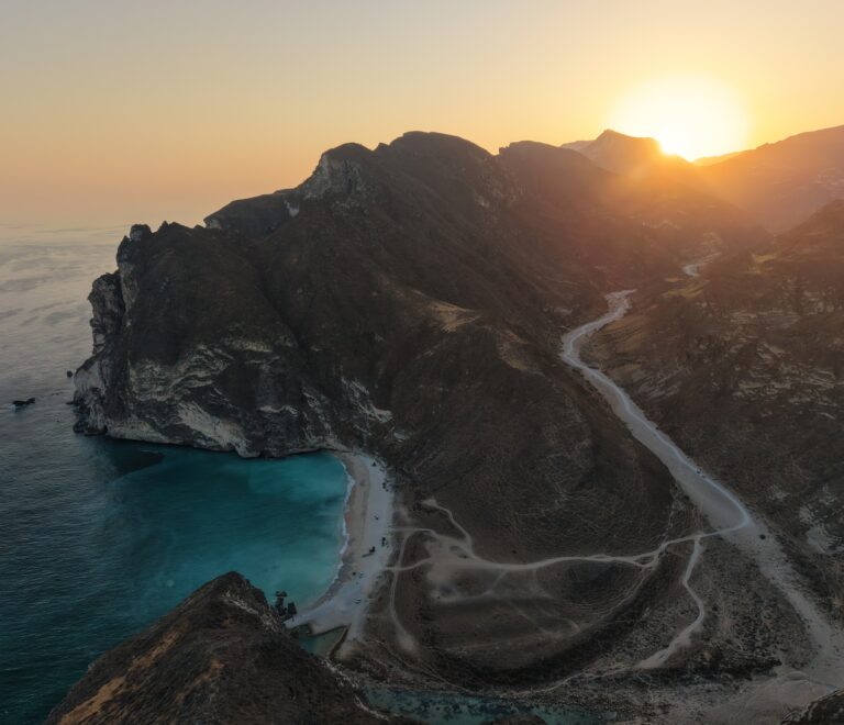 Hidden Beach Salalah Oman sunset view with mountains, turquoise sea, and scenic coastal road